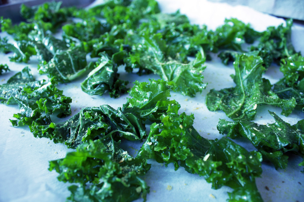 Uncooked massaged kale tossed with applewood smoked sea salt and nutritional yeast, spread out on parchment paper